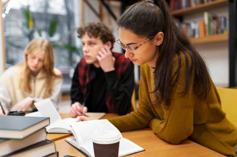 Un grupo de estudiantes está estudiando juntos en una mesa, con libros y una taza de café.