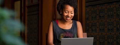 Una mujer sonriente trabaja en su laptop en un ambiente acogedor.