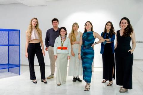 Un grupo de siete personas posando en una sala moderna con una obra artística al fondo.