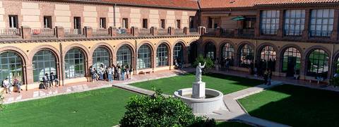 Un patio con una fuente en el centro y grupos de personas conversando alrededor.