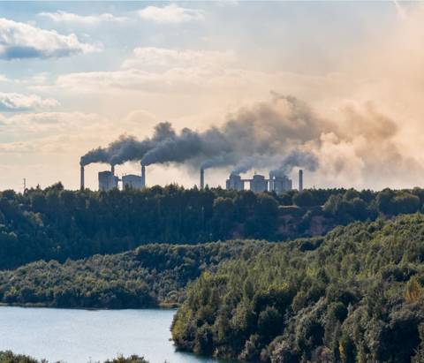Una vista de una planta industrial emitiendo humo sobre un paisaje natural.