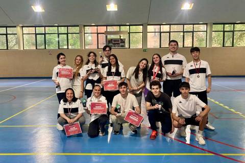 Un grupo de jóvenes sosteniendo trofeos y diplomas en un gimnasio después de un evento deportivo.