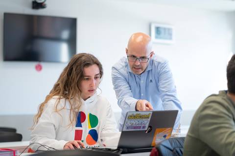Un profesor ayuda a una estudiante en una lección frente a un ordenador portátil.