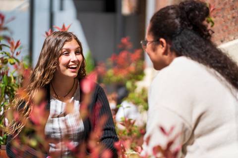 Dos mujeres sonríen y conversan en un entorno al aire libre rodeadas de plantas.