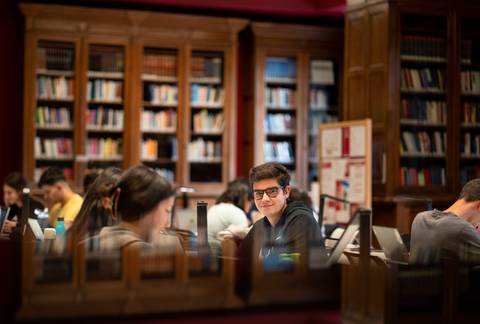 Un grupo de estudiantes se encuentra estudiando en una biblioteca con estanterías llenas de libros.