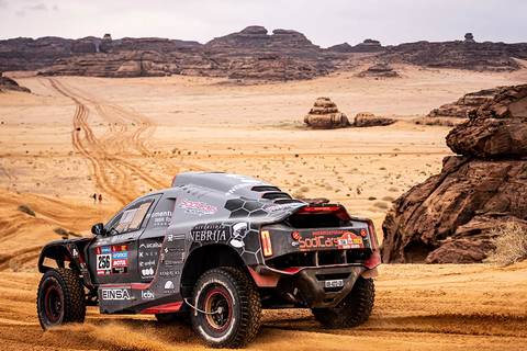 Un vehículo todoterreno surca un desierto con formaciones rocosas al fondo.