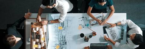 Un grupo de personas trabajando en un proyecto sobre una mesa llena de planos y maquetas.