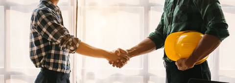 Dos personas estrechándose la mano en un ambiente laboral con un casco de construcción amarillo.