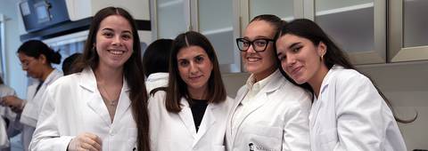 Cuatro jóvenes sonrientes en un laboratorio vestidos con batas blancas.