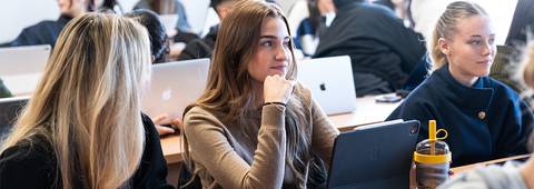 Un grupo de estudiantes presta atención en un aula con computadoras portátiles.