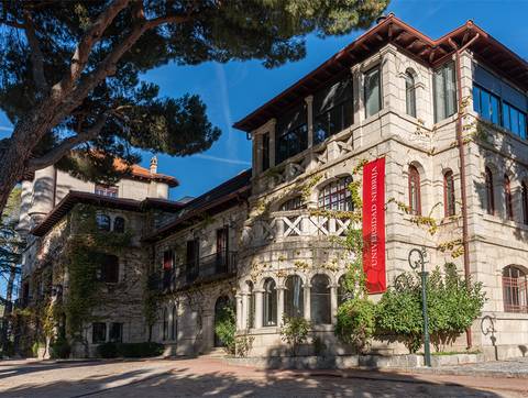 Edificio de estilo arquitectónico con vegetación que lo rodea y un cartel de la Universidad de Nebrija.