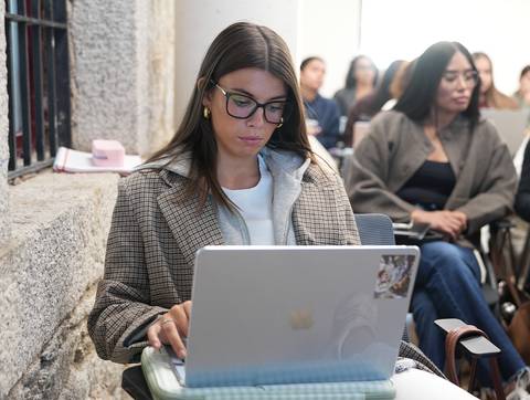 Una mujer con gafas está usando una computadora portátil en un ambiente de clase.