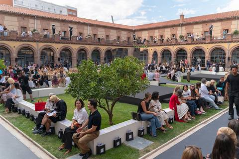 Una gran multitud se reúne en un patio al aire libre, disfrutando de un evento social con áreas verdes y asientos cómodos.
