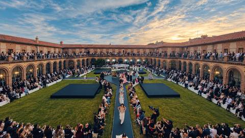 Una pasarela de moda al aire libre con un público atento rodeando el evento durante una hermosa puesta de sol.