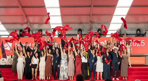 Estudiantes celebran su graduación lanzando cintas rojas en un evento festivo.