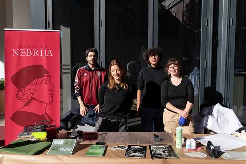 Un grupo de cuatro personas posan junto a una mesa con material educativo y un cartel de la Fundación Nebrija.
