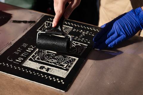 Una mano aplica tinta negra sobre una plancha de grabado con un rodillo.