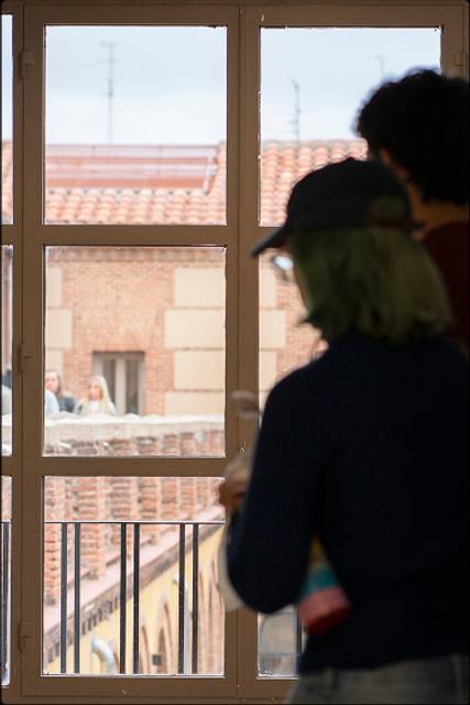 Una persona observa por una ventana mientras otros están al aire libre.