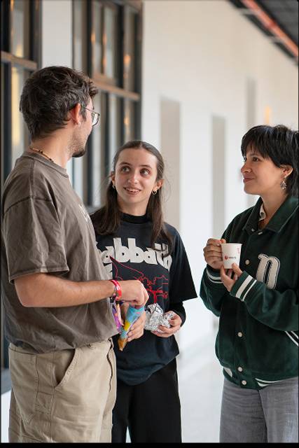 Tres personas conversan en un pasillo, compartiendo un momento amigable.