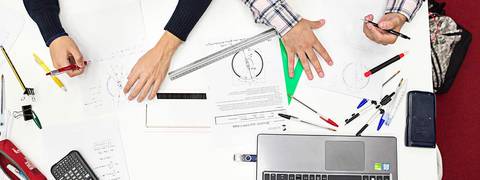 Una mesa de estudio con manos y material de oficina disperso sobre ella.