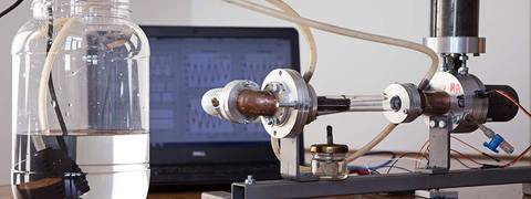 La imagen muestra un equipo experimental para medir fluidos, compuesto por un recipiente con agua y un sistema de tuberías conectado a una computadora.