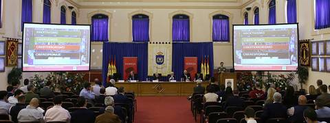 Una conferencia en un salón con pantallas que muestran información y un público atento.