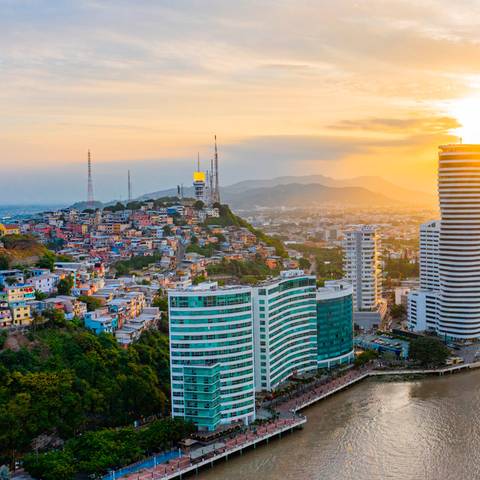 Vista panorámica de una ciudad costera al atardecer, con edificios y colinas iluminadas por el sol.