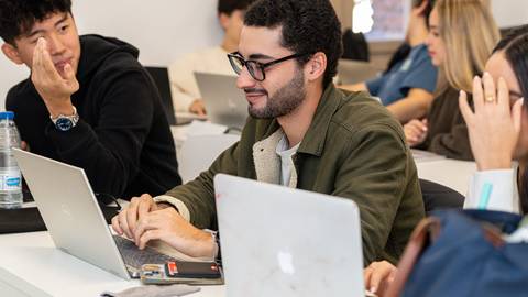 Un grupo de estudiantes en un aula, centrados en sus computadoras portátiles.