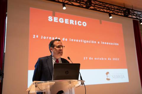 Un hombre presenta un evento titulado '2ª Jornada de investigación e innovación' con un fondo rojo.