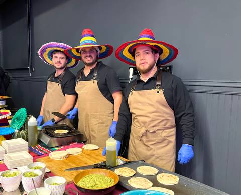 Tres hombres en sombreros de charro están preparando comida en un evento festivo.