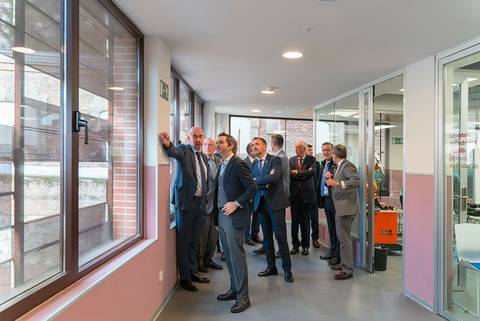 Un grupo de hombres en trajes de negocio se encuentra en un pasillo, observando por la ventana mientras uno de ellos señala algo.