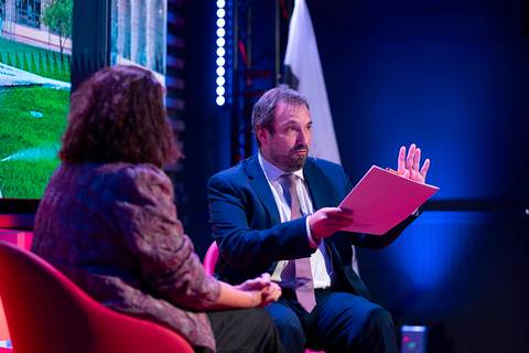 Un hombre y una mujer están conversando en un escenario durante un evento.