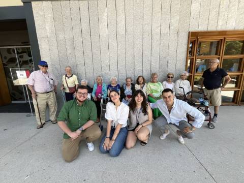Un grupo de personas mayores y jóvenes posando juntos frente a un edificio.