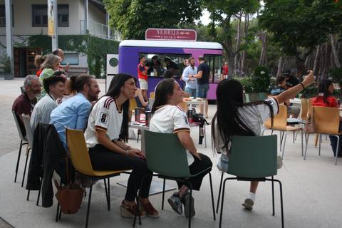 Un grupo de personas se sienta en una mesa mientras observan y disfrutan de un evento en un entorno al aire libre.