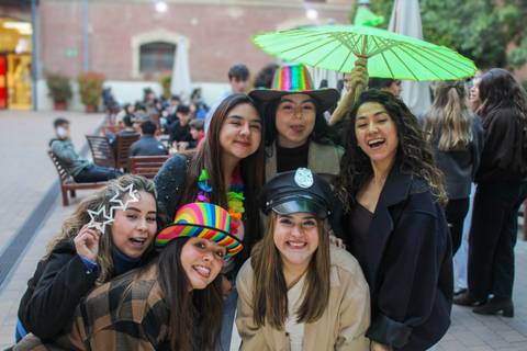 Un grupo de amigas posando sonrientes con sombreros y accesorios coloridos en un ambiente festivo al aire libre.