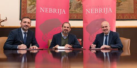 Tres hombres se encuentran firmando documentos frente a banners de la Universidad Nebrija.