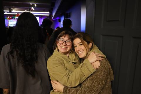 Dos mujeres sonrientes se abrazan en un ambiente festivo y lleno de gente.