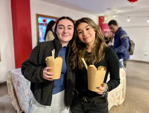 Dos jóvenes están sonriendo mientras sostienen recipientes de comida en un ambiente social.