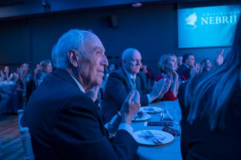 Un grupo de personas aplaudiendo en un evento formal con una iluminación tenue.