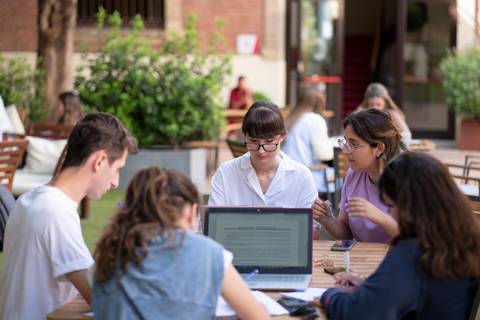 Un grupo de estudiantes trabaja en una mesa al aire libre, concentrados en sus laptops y papeles.