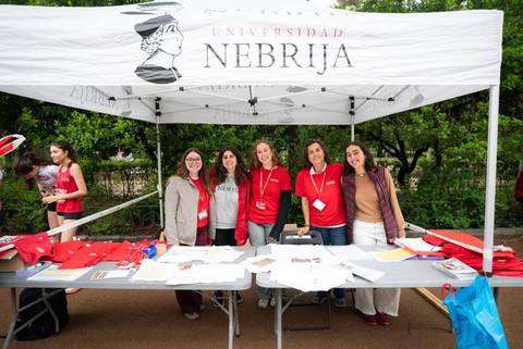 Un grupo de cinco personas sonrientes se encuentra en un stand de la Universidad Nebrija durante un evento al aire libre.