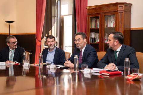 Una reunión en una sala con cuatro hombres sentados alrededor de una mesa de madera.