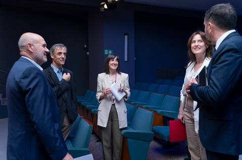 Un grupo de cinco personas conversando en una sala vacía con asientos verdes.