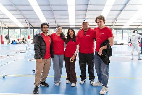Un grupo de cinco personas sonrientes vestidas con camisetas rojas en un ambiente deportivo.