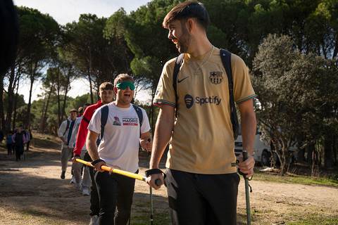 Un grupo de jóvenes camina por un sendero en un entorno natural, algunos utilizan accesorios como bastones.
