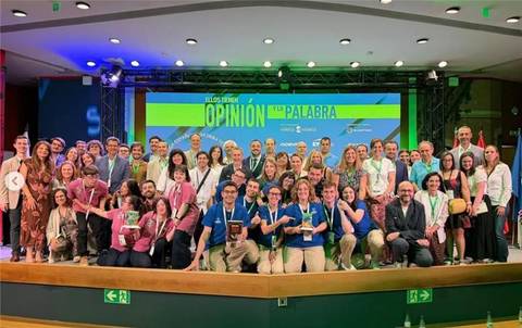 Un grupo diverso de personas sonríe en un evento, posando para una foto grupal frente a un escenario iluminado.