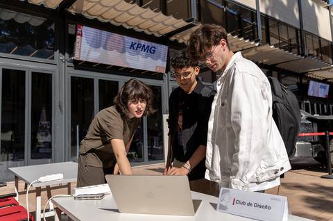 Tres jóvenes interactúan alrededor de una computadora portátil en un evento al aire libre.