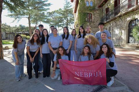 Un grupo de jóvenes se reúne al aire libre sosteniendo una bandera de la Fundación Nebrija.