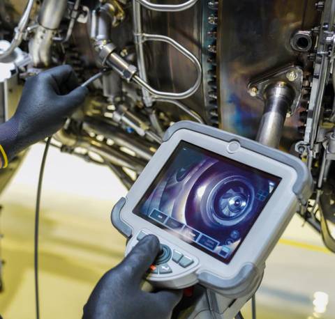 Una persona está revisando el interior de un motor con una pantalla de monitorización.