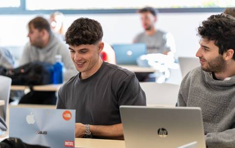 Un grupo de estudiantes se encuentra en un aula utilizando computadoras portátiles.